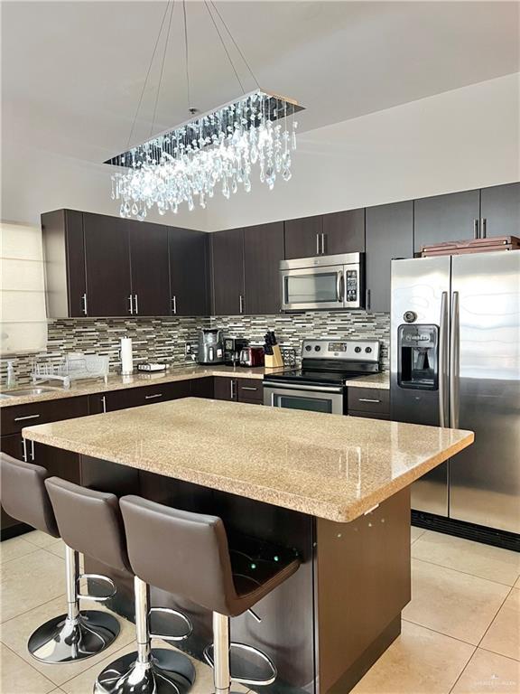 kitchen with appliances with stainless steel finishes, light tile patterned floors, a kitchen island, and a breakfast bar area