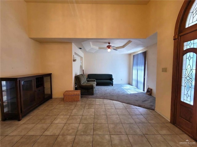 entryway with light carpet, a towering ceiling, a raised ceiling, and ceiling fan