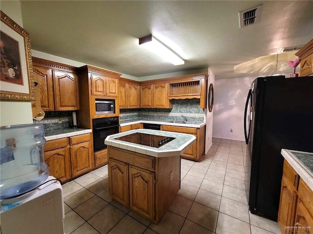 kitchen with light tile patterned floors, a kitchen island, tile counters, and black appliances