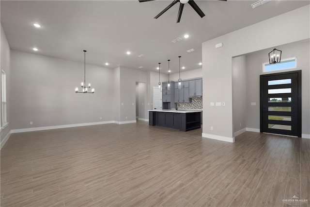 unfurnished living room with hardwood / wood-style floors, ceiling fan with notable chandelier, and sink