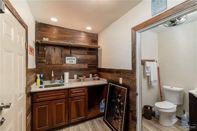 bar with light stone countertops, sink, dark brown cabinets, and light hardwood / wood-style flooring