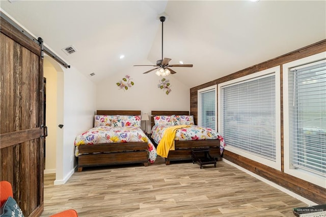 bedroom with ceiling fan, a barn door, vaulted ceiling, and light hardwood / wood-style flooring