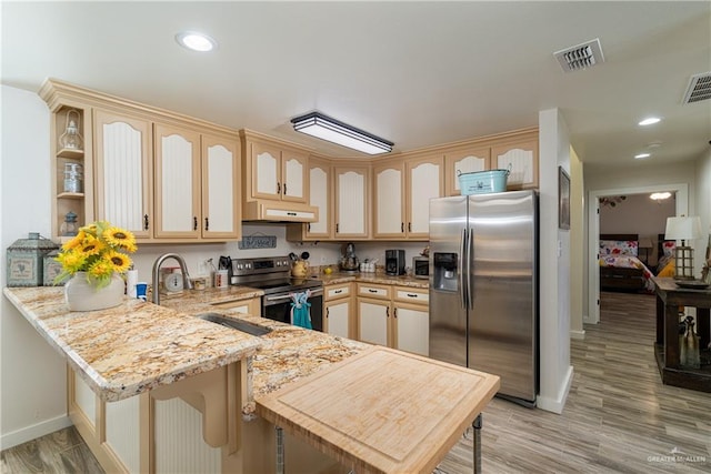 kitchen with light brown cabinets, light stone counters, kitchen peninsula, and appliances with stainless steel finishes