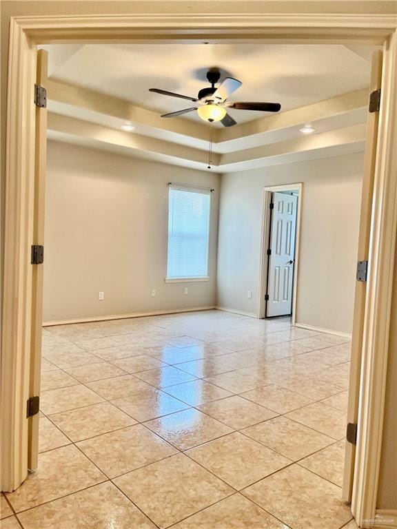 empty room featuring a tray ceiling, baseboards, a ceiling fan, and light tile patterned floors