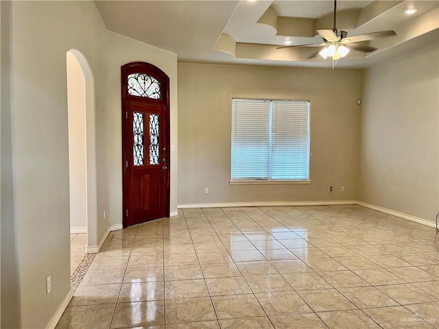 foyer entrance with ceiling fan, a raised ceiling, arched walkways, and baseboards