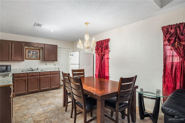 dining area with a textured ceiling, a notable chandelier, and sink