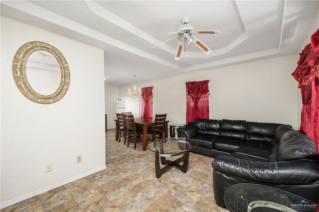 living room with ceiling fan with notable chandelier and a tray ceiling