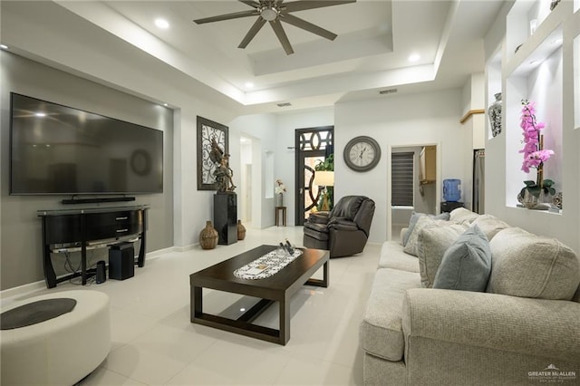 tiled living room with ceiling fan and a tray ceiling