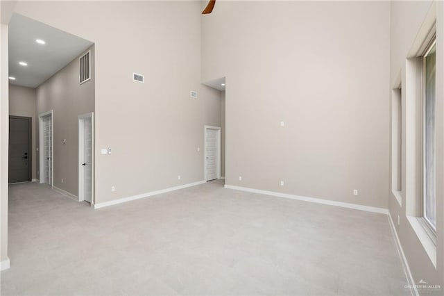 interior space with ceiling fan, a towering ceiling, and light carpet