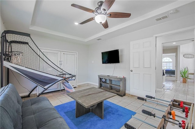 living area featuring a ceiling fan, a tray ceiling, tile patterned flooring, baseboards, and recessed lighting