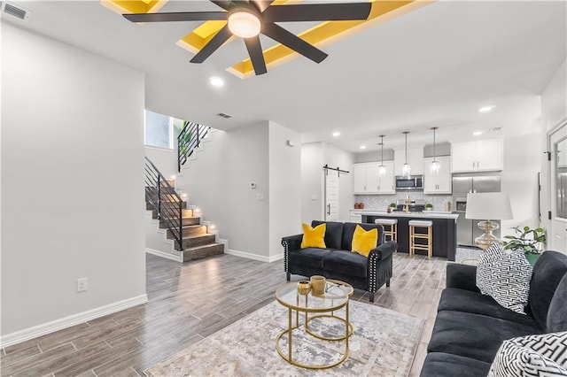 living area with a barn door, stairway, light wood-style flooring, and visible vents