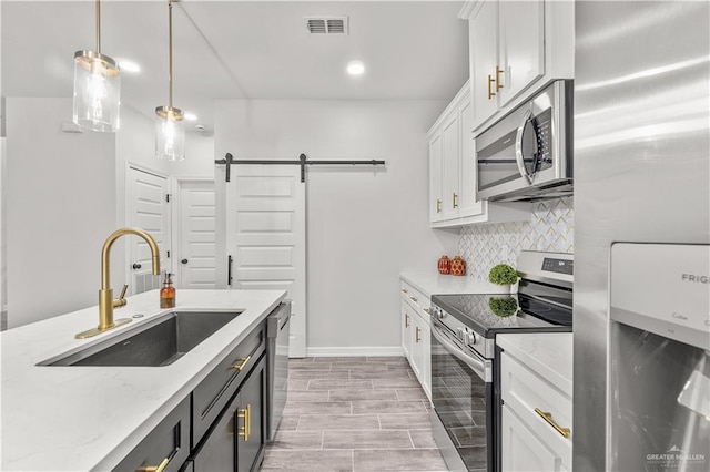 kitchen featuring a barn door, a sink, visible vents, appliances with stainless steel finishes, and backsplash