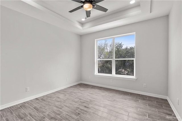 spare room featuring a raised ceiling, ceiling fan, baseboards, and wood finished floors