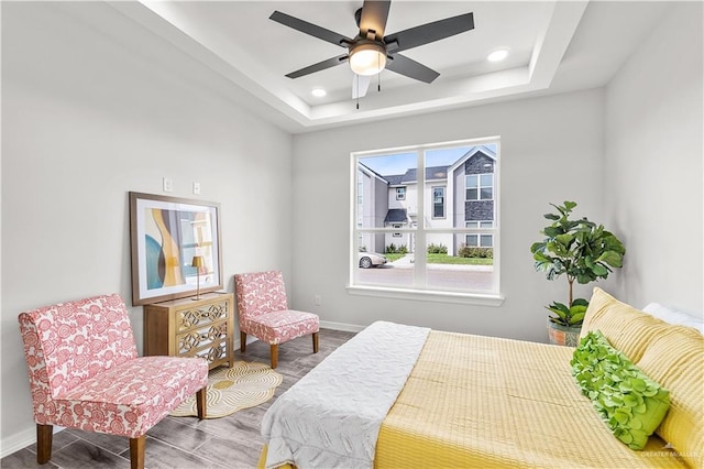 bedroom featuring a tray ceiling, wood finished floors, baseboards, and recessed lighting