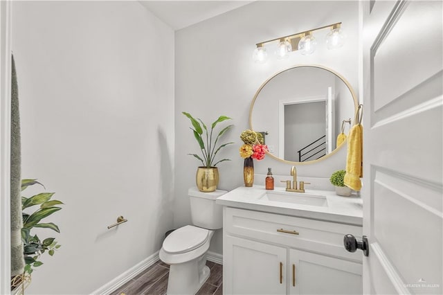 half bathroom featuring wood finish floors, baseboards, vanity, and toilet