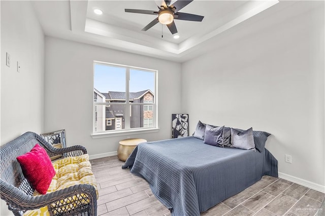 bedroom featuring wood finish floors, a raised ceiling, baseboards, and recessed lighting