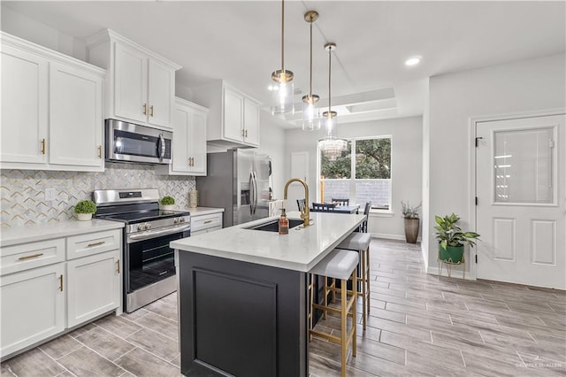 kitchen with tasteful backsplash, a center island with sink, appliances with stainless steel finishes, white cabinetry, and a sink