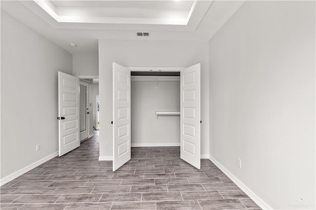 unfurnished bedroom with wood finish floors, visible vents, baseboards, a closet, and a raised ceiling