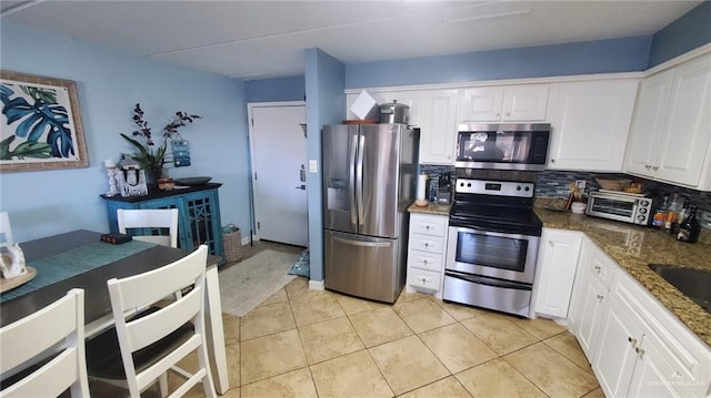 kitchen featuring white cabinets, backsplash, appliances with stainless steel finishes, and dark stone counters