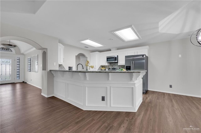 kitchen with white cabinetry, dark hardwood / wood-style floors, stainless steel appliances, and kitchen peninsula