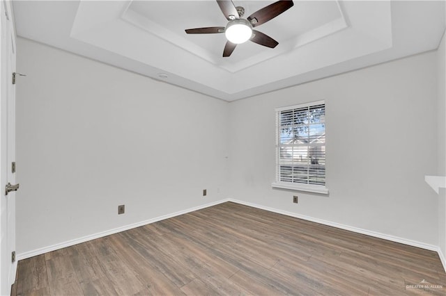 empty room with hardwood / wood-style floors, a raised ceiling, and ceiling fan