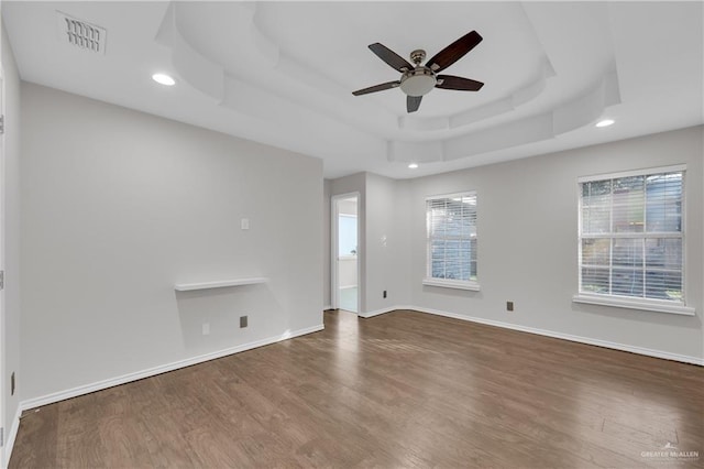 empty room with ceiling fan, a raised ceiling, and hardwood / wood-style floors