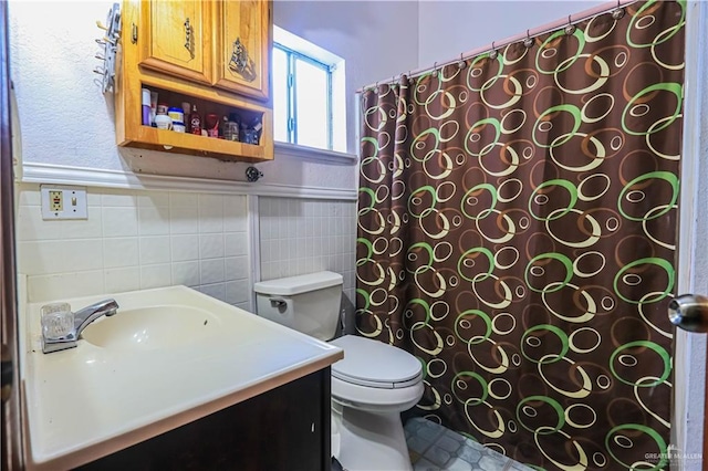 full bathroom featuring a shower with curtain, tile walls, vanity, toilet, and wainscoting