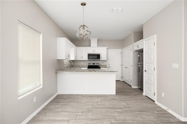 kitchen featuring light wood-type flooring, a sink, a peninsula, appliances with stainless steel finishes, and a chandelier