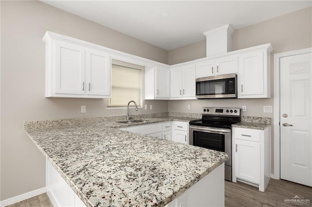 kitchen with a peninsula, a sink, light wood-style floors, appliances with stainless steel finishes, and white cabinetry