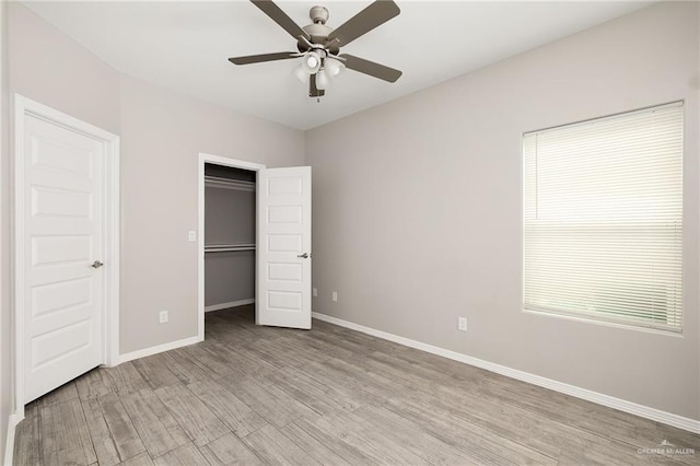 unfurnished bedroom with a ceiling fan, baseboards, light wood-style flooring, a closet, and a walk in closet