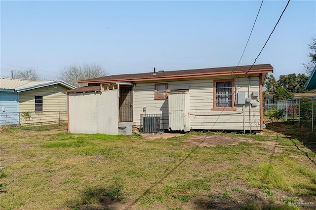 back of house with central AC unit, fence, a lawn, and an outbuilding