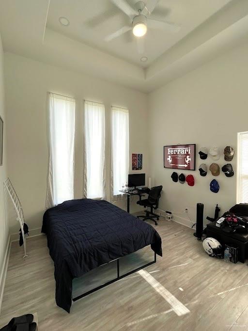 bedroom featuring light wood finished floors, ceiling fan, a tray ceiling, and baseboards