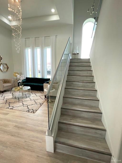 stairs featuring recessed lighting, a raised ceiling, an inviting chandelier, wood finished floors, and baseboards