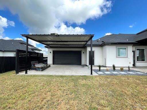 back of house with a garage, fence, a lawn, and stucco siding