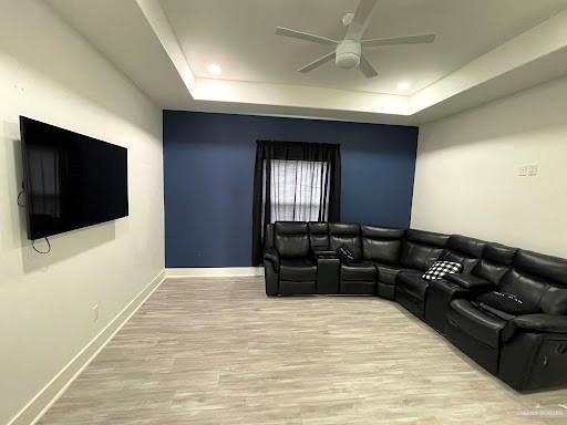 living area with a tray ceiling, ceiling fan, baseboards, and wood finished floors