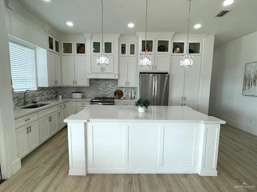 kitchen with a kitchen island, a sink, light countertops, appliances with stainless steel finishes, and tasteful backsplash