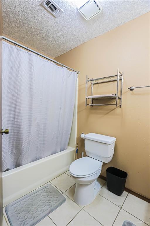 bathroom featuring tile patterned flooring, shower / tub combo, a textured ceiling, and toilet