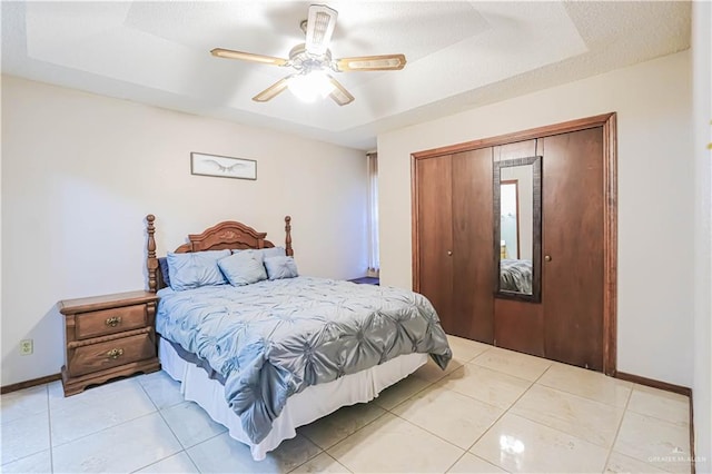 tiled bedroom with a closet, a tray ceiling, and ceiling fan