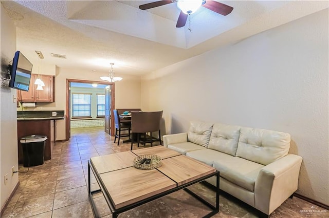 tiled living room with ceiling fan with notable chandelier and a textured ceiling