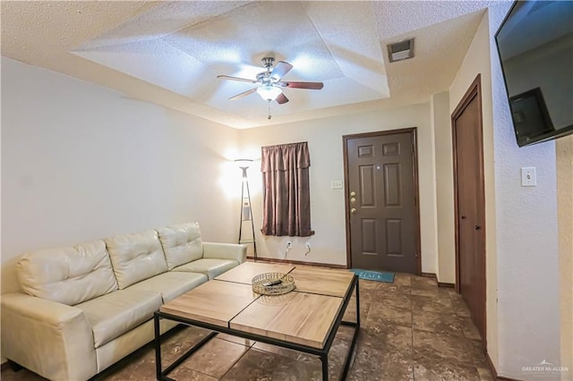 living room featuring ceiling fan, a raised ceiling, and a textured ceiling