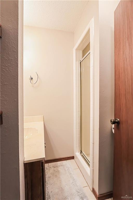 bathroom with tile patterned floors, vanity, an enclosed shower, and a textured ceiling