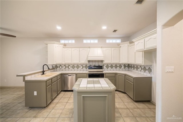 kitchen featuring tile counters, a center island, premium range hood, kitchen peninsula, and appliances with stainless steel finishes