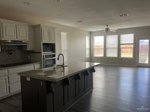 14405 Chalk Ridge Dr, Mcallen, TX 78504 - kitchen with stainless steel oven, black electric cooktop, under cabinet range hood, dark wood finished floors, and a kitchen island with sink