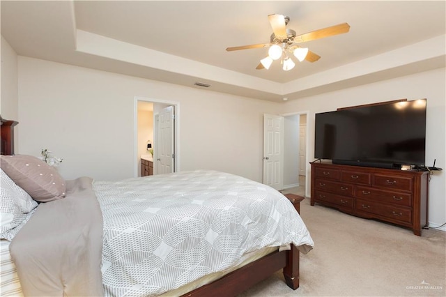 carpeted bedroom with a raised ceiling, ensuite bath, and ceiling fan