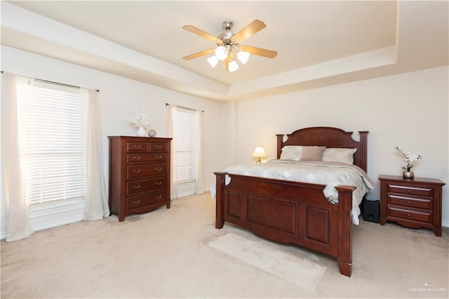 carpeted bedroom with ceiling fan, a raised ceiling, and multiple windows