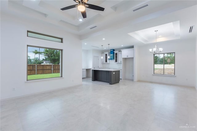 unfurnished living room featuring ceiling fan with notable chandelier and a raised ceiling