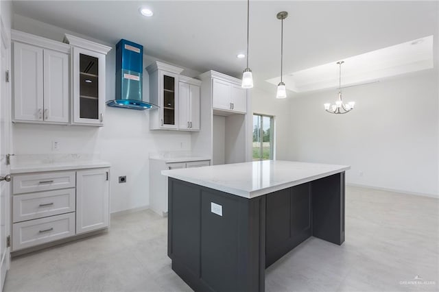 kitchen featuring white cabinetry, a center island, wall chimney range hood, a notable chandelier, and decorative light fixtures