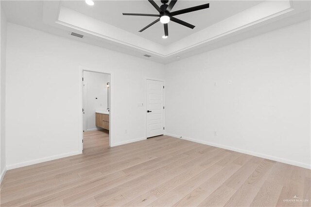 unfurnished bedroom featuring a raised ceiling, ensuite bath, light hardwood / wood-style flooring, and ceiling fan