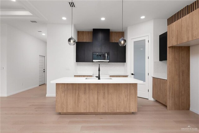 kitchen with pendant lighting, a center island with sink, sink, and light hardwood / wood-style flooring