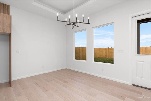 unfurnished dining area featuring a chandelier, light wood-type flooring, and a tray ceiling